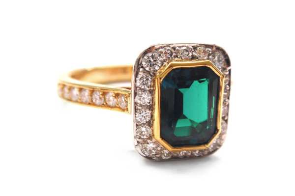 Emerald cut emerald, bezel set with halo of brilliant cut diamonds surrounding and a yellow gold pave set diamond band
