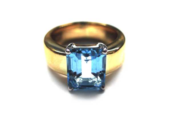 Emerald cut light blue topaz claw set over wide yellow gold band