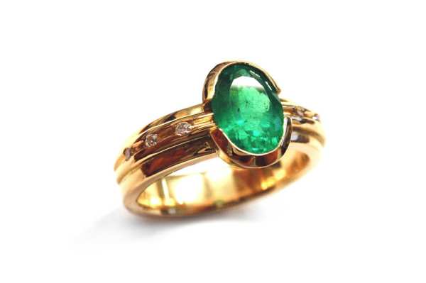 Oval natural emerald split bezel set with small brilliant diamonds set into yellow gold band