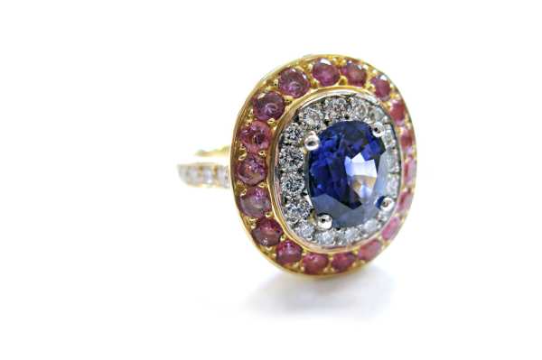 Claw set blue sapphire with surrounding halo of brilliant cut diamonds and pink coloured sapphires pave set with diamond band