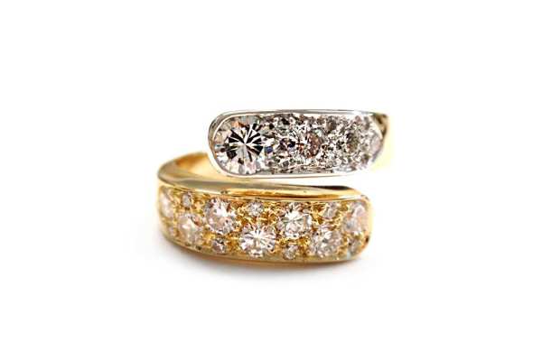 Multi sized round brilliant cut diamonds set into the ends of yellow and white gold cross over band