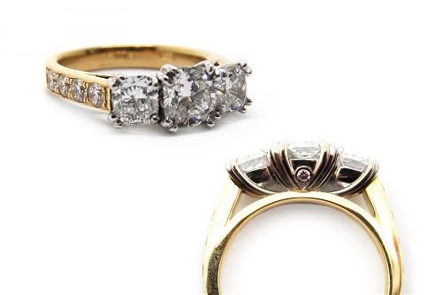 White gold diamond cushion cut three stone engagement ring, with small diamonds in the band and pink diamonds in the underrail