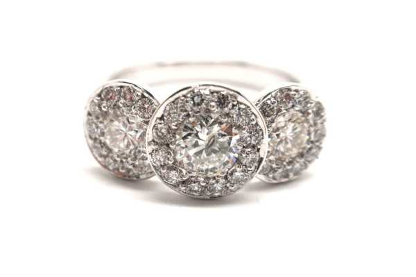 Three brilliant cut round diamonds surrounded with smaller round diamonds pave set into white gold band