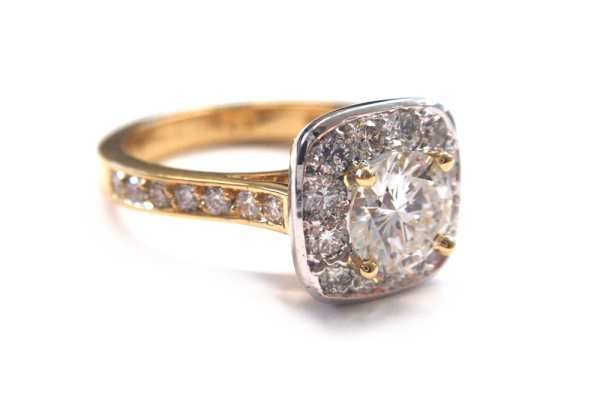 Brilliant cut round diamond claw set with smaller diamonds halo set in a cushion cut shape with pave diamonds in band