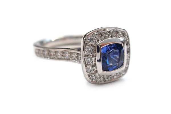 Cushion cut blue sapphire bezel set with a halo of pave diamonds 