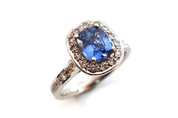 Cushion cut blue sapphire claw set with surrounding white round diamonds pave set